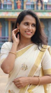 Woman wearing a traditional Kerala kasavu saree with elegant gold jewellery and subtle temple look makeup by Saranya, featuring natural glowing skin, soft eye makeup, nude lips, and a classic bindi, photographed in a South Indian temple background.